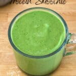 Spinach protein smoothie in a glass cup on wooden counter with black and white tea towel, text overlay reads ‘Spinach Protein Smoothie – Healthy, Creamy & Delicious’