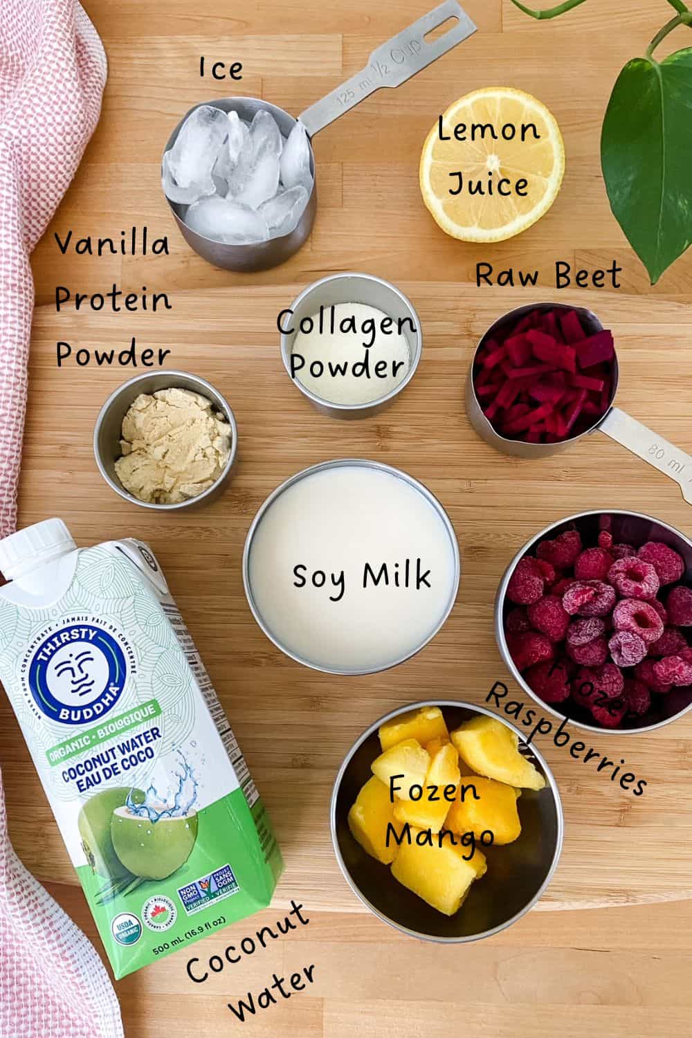 Overhead photo of beet protein smoothie ingredients on a wooden surface, including soy milk, frozen raspberries, frozen mango, raw beet, lemon juice, coconut water, vanilla protein powder, collagen powder, and ice.