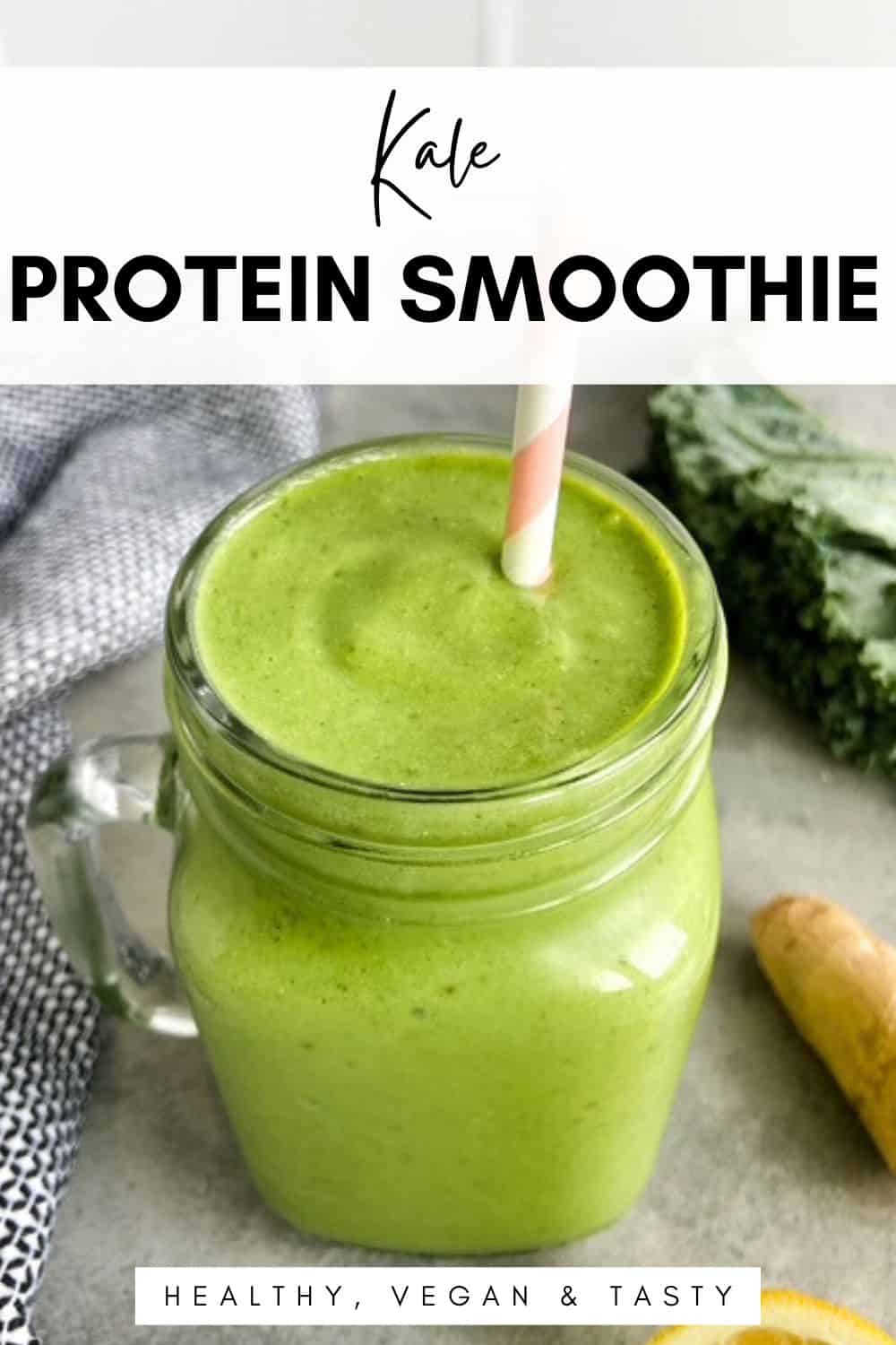 Green kale protein smoothie in a glass mason jar with a striped paper straw, fresh kale, ginger, and lemon on a light countertop
