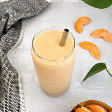 Peach protein smoothie made with frozen peaches, banana, soy milk, protein powder, and spices in a glass with a metal straw