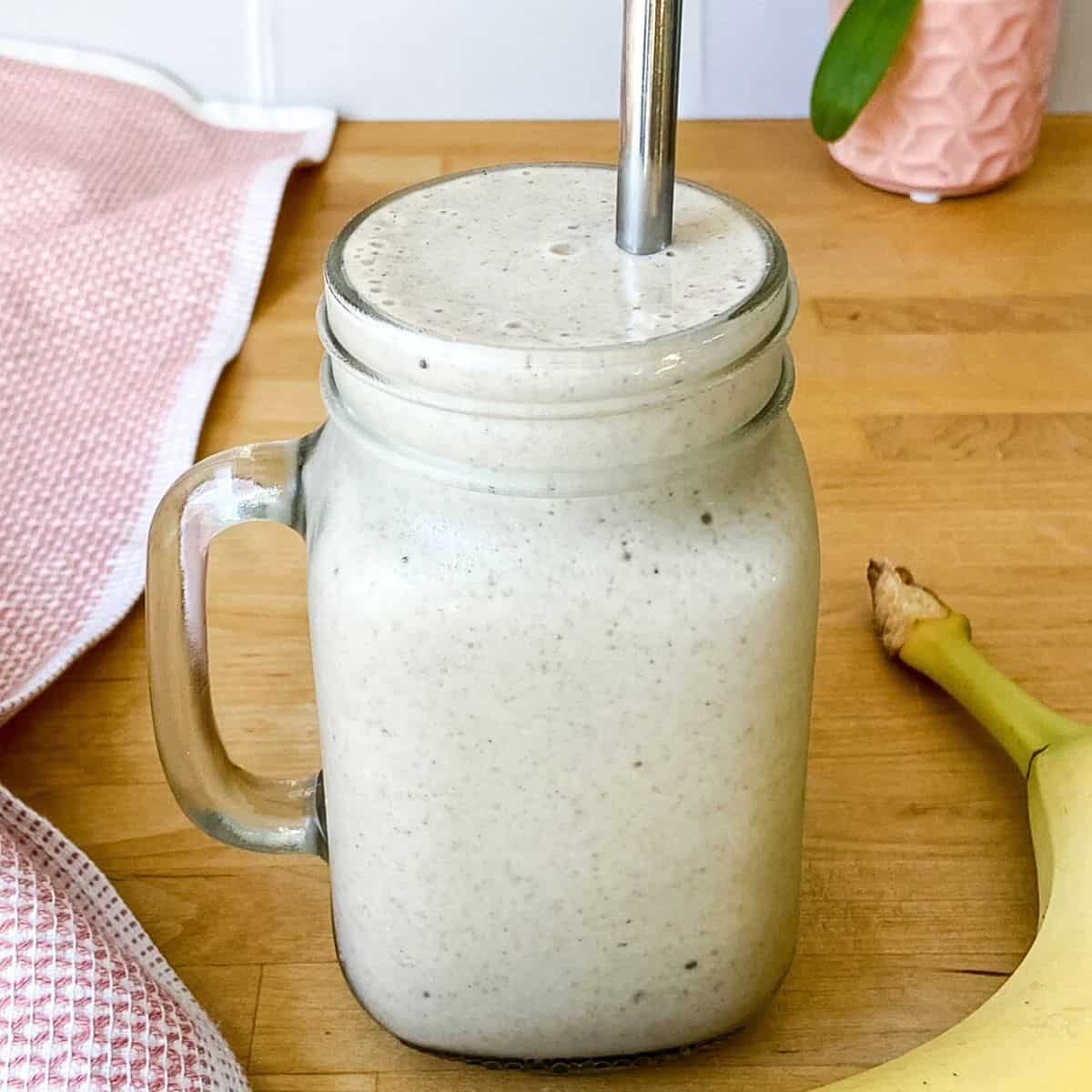 banana protein smoothie with cinnamon and nutmeg in a glass mason jar with metal straw on a wooden counter.