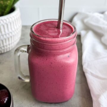 Cherry yogurt smoothie in a glass mason jar with a straw, with a plant and white tea towel in the background