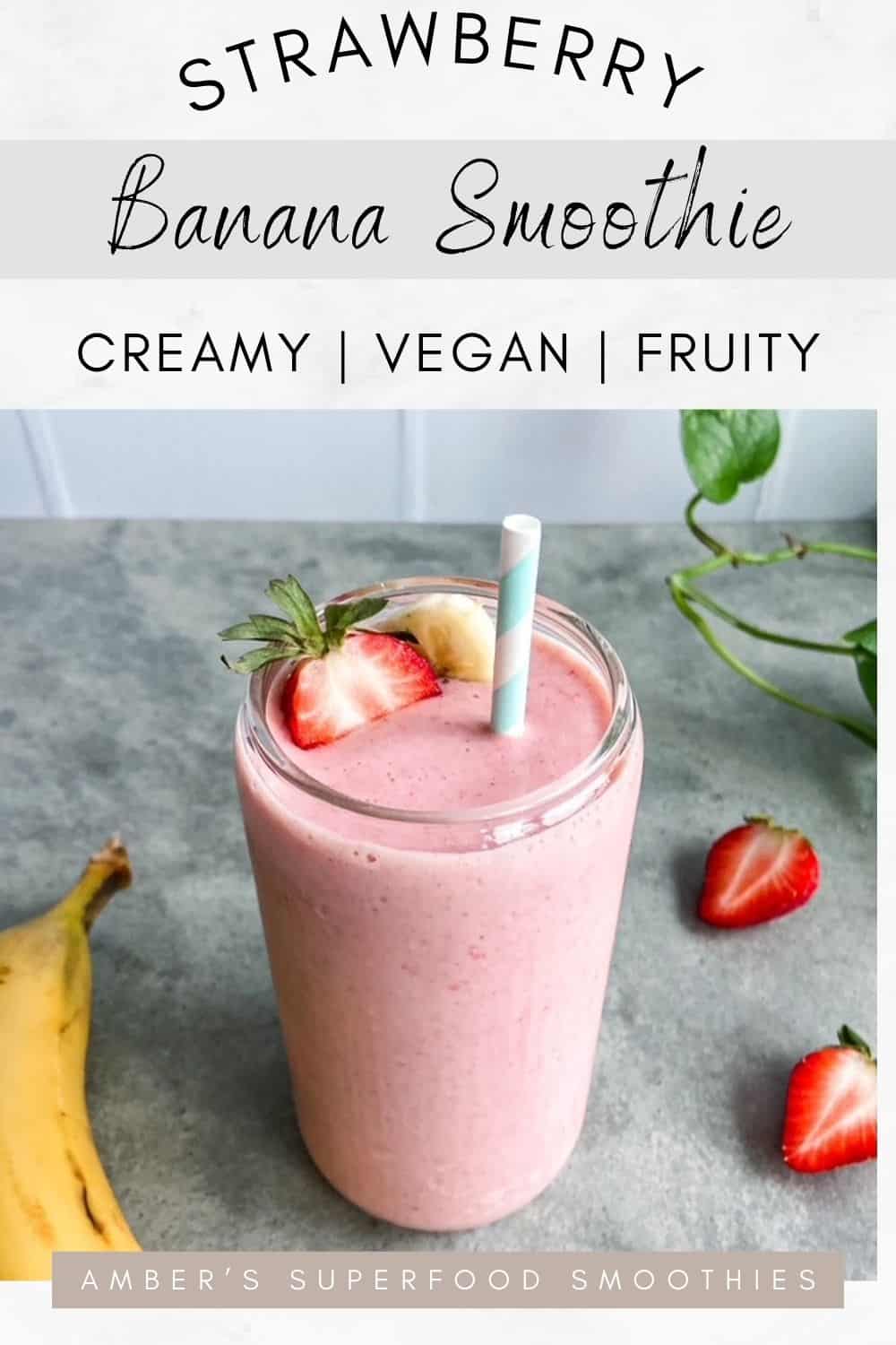 A glass of creamy pink smoothie topped with a fresh strawberry and banana slice, sitting on a grey surface with whole strawberries and a banana in the background.
