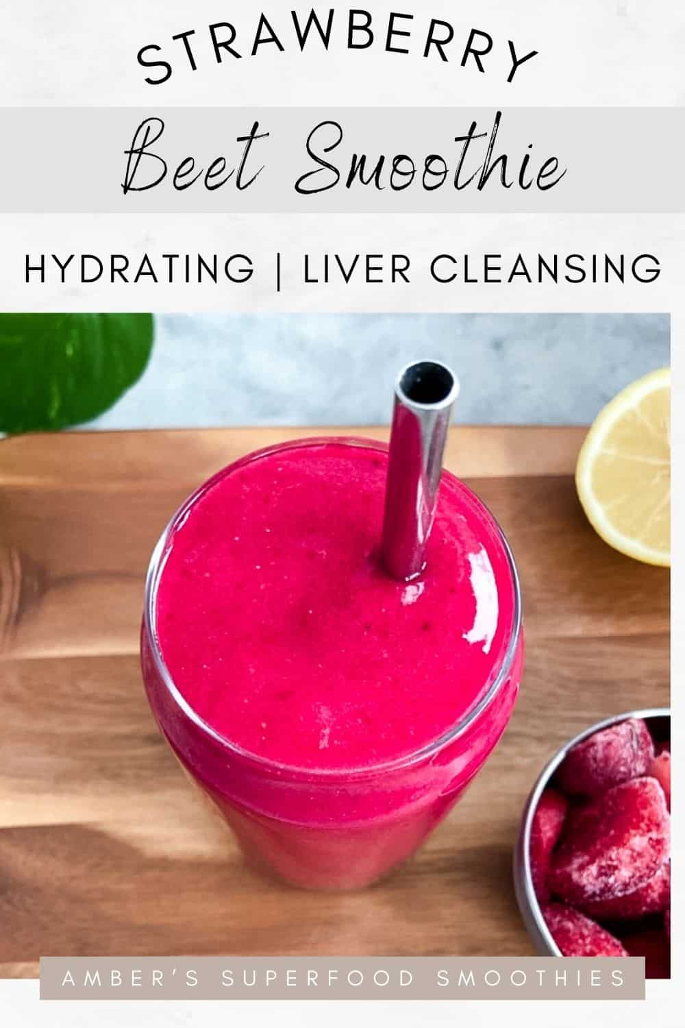 Bright pink smoothie in a clear glass with a metal straw on a wooden board, with lemon and frozen fruit nearby.