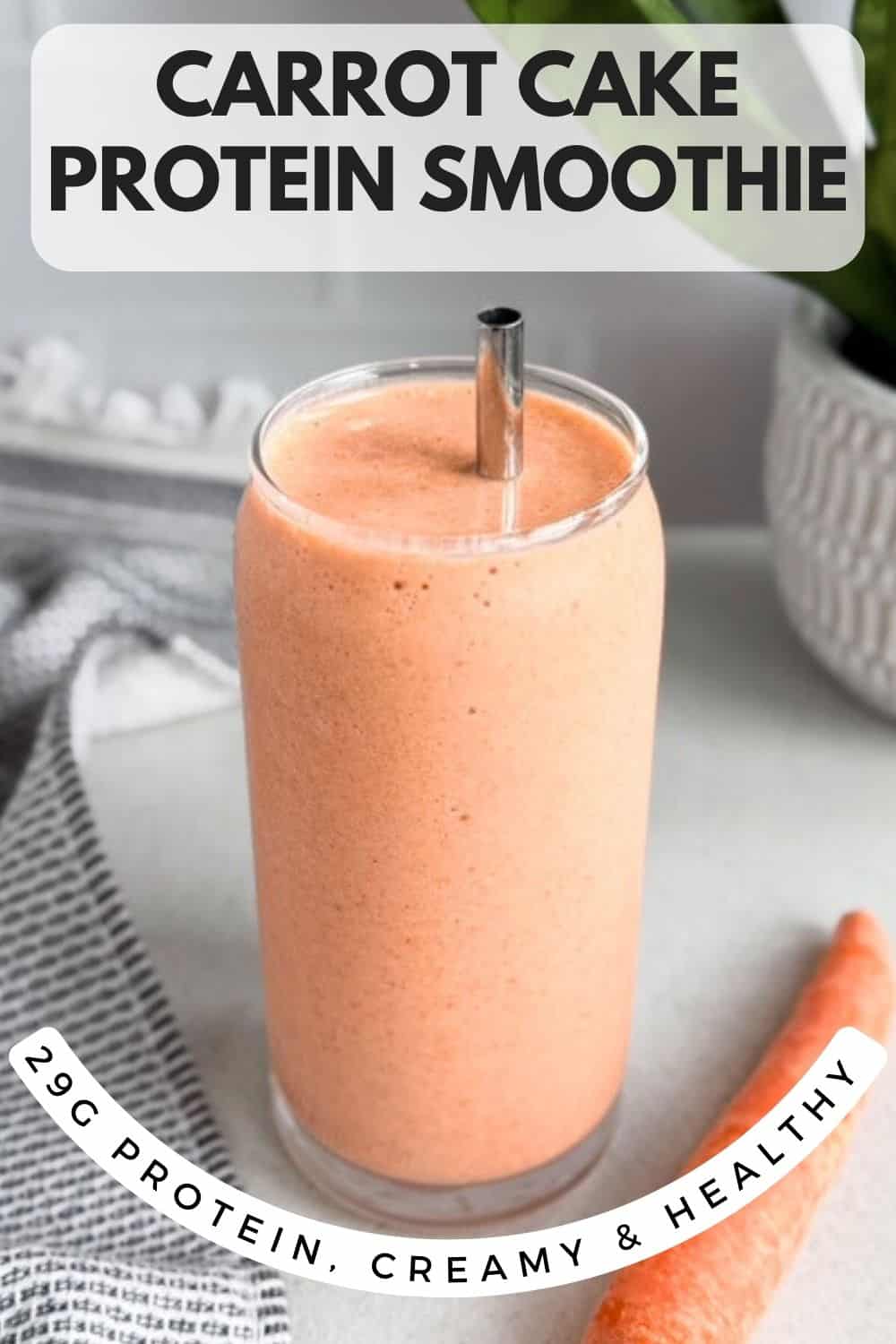 Carrot cake protein smoothie in a tall glass with a metal straw and a whole carrot beside it with text overlay describing 32 g protein creamy healthy smoothie
