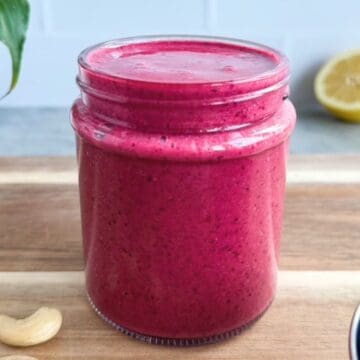 Cherry smoothie in a glass jar on a wooden board with cashews and a lemon in the background