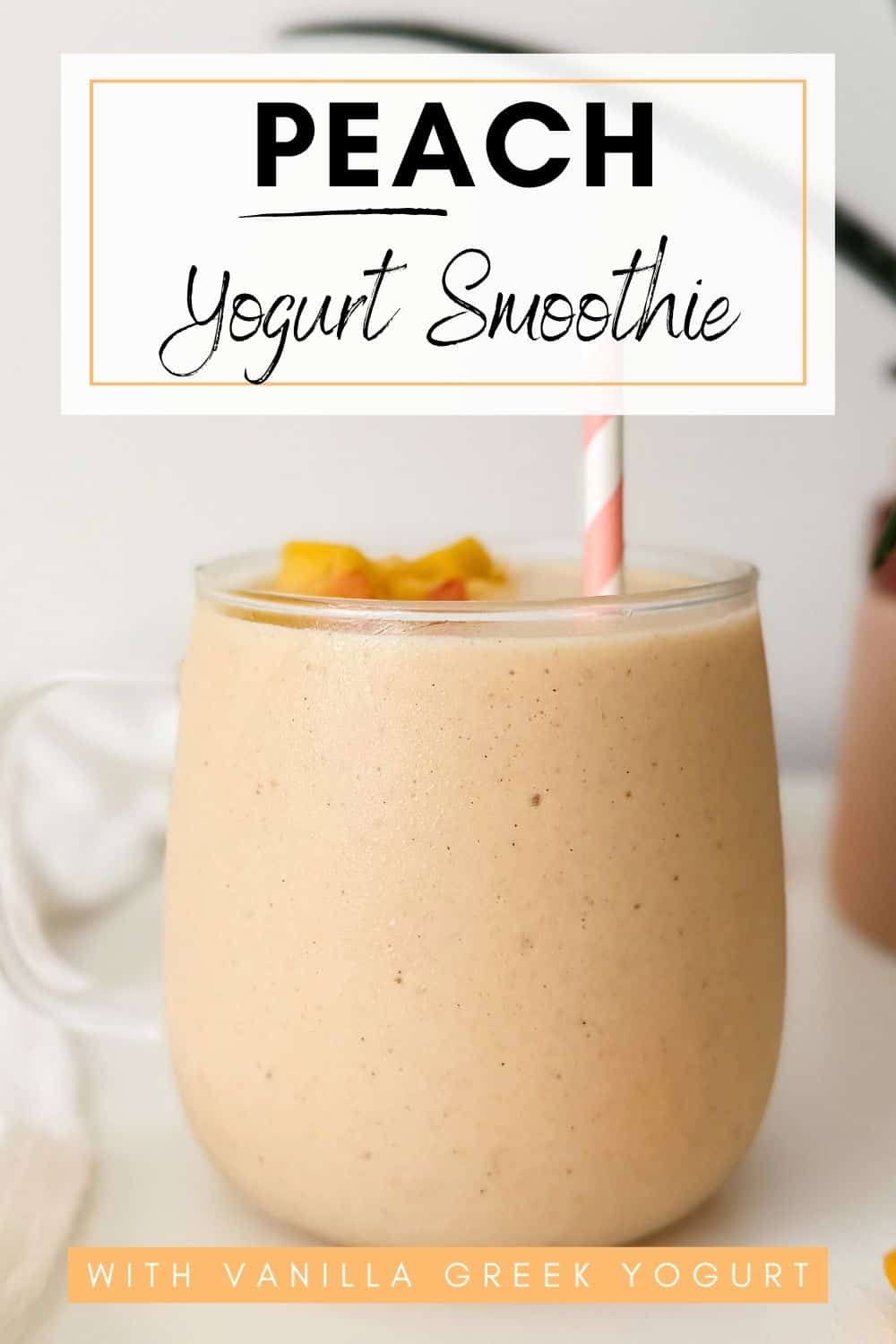 Creamy peach yogurt smoothie topped with peach pieces in a glass with a pink striped straw.